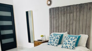 A modern bedroom with a large bed, a wooden headboard, a nightstand with a lamp, and a wall-mounted clock. - HOTEL BUNGALOWS CASA BLANCA (Tenancingo)