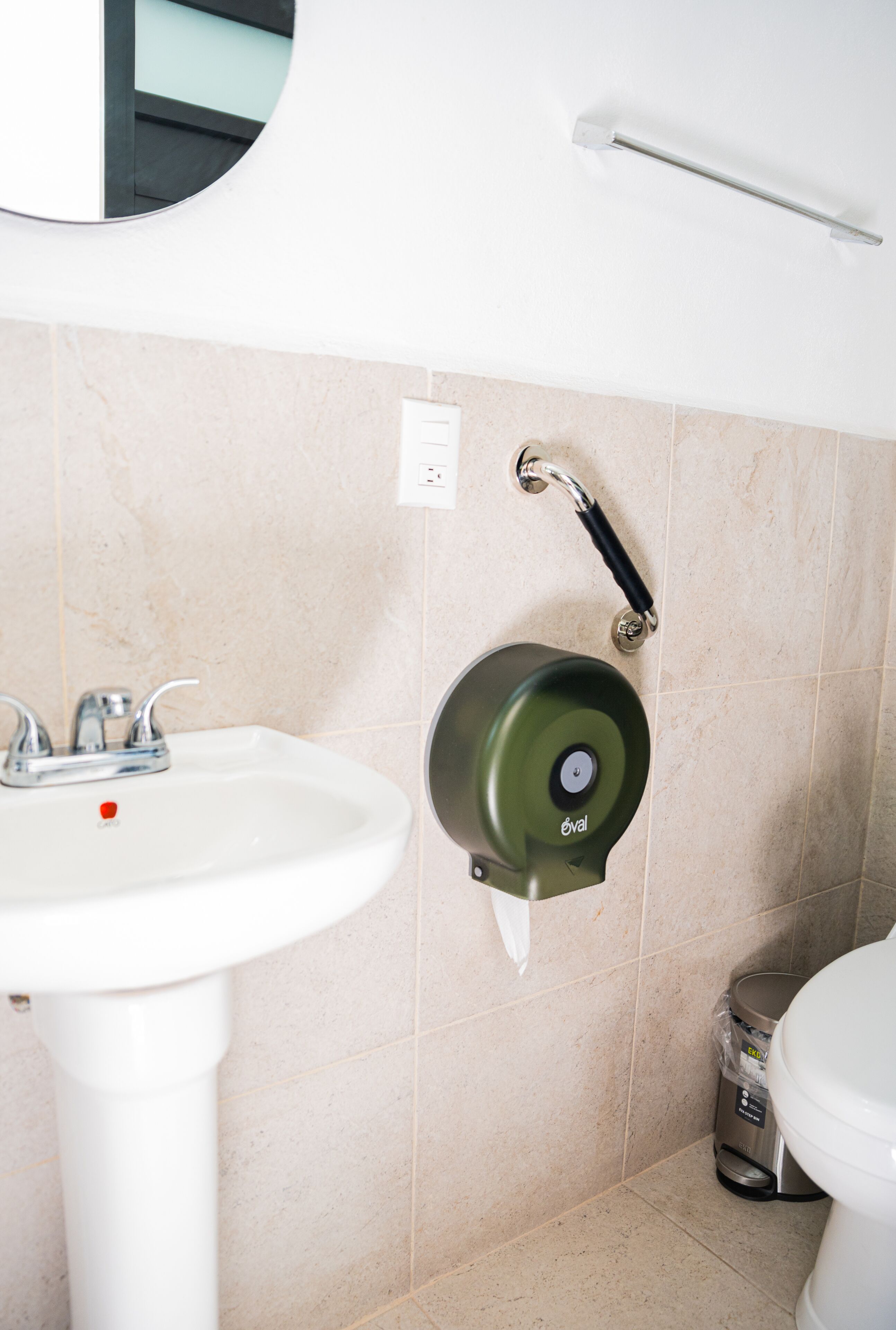 A bathroom with a white sink, a toilet, and a paper towel dispenser mounted on the wall.