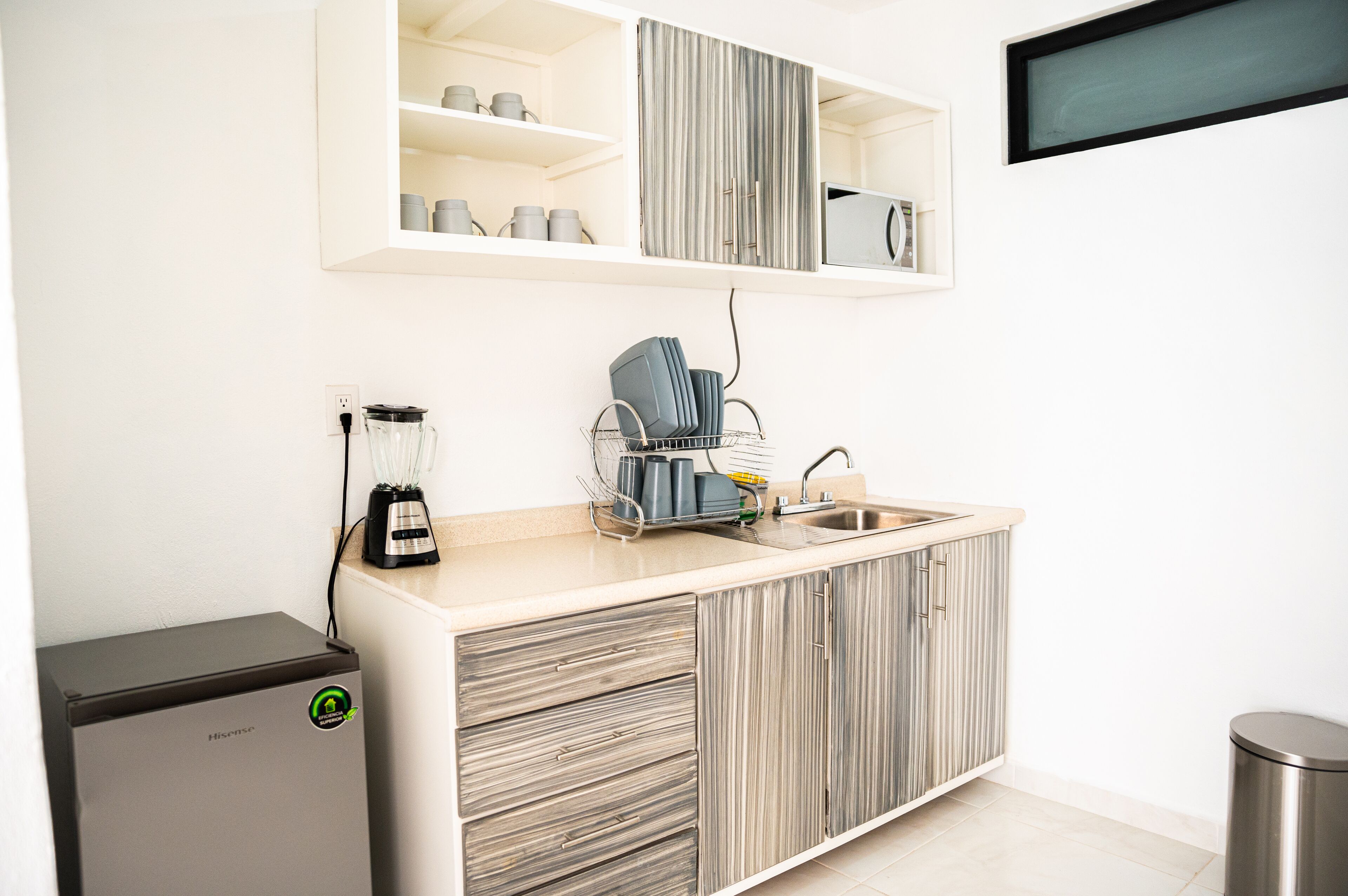 A compact kitchenette with a built-in refrigerator, a coffee maker, and a sink.