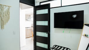 A room with a sliding door leading to a kitchen, a black metal chair, and a wall-mounted TV. - HOTEL BUNGALOWS CASA BLANCA (Tenancingo)