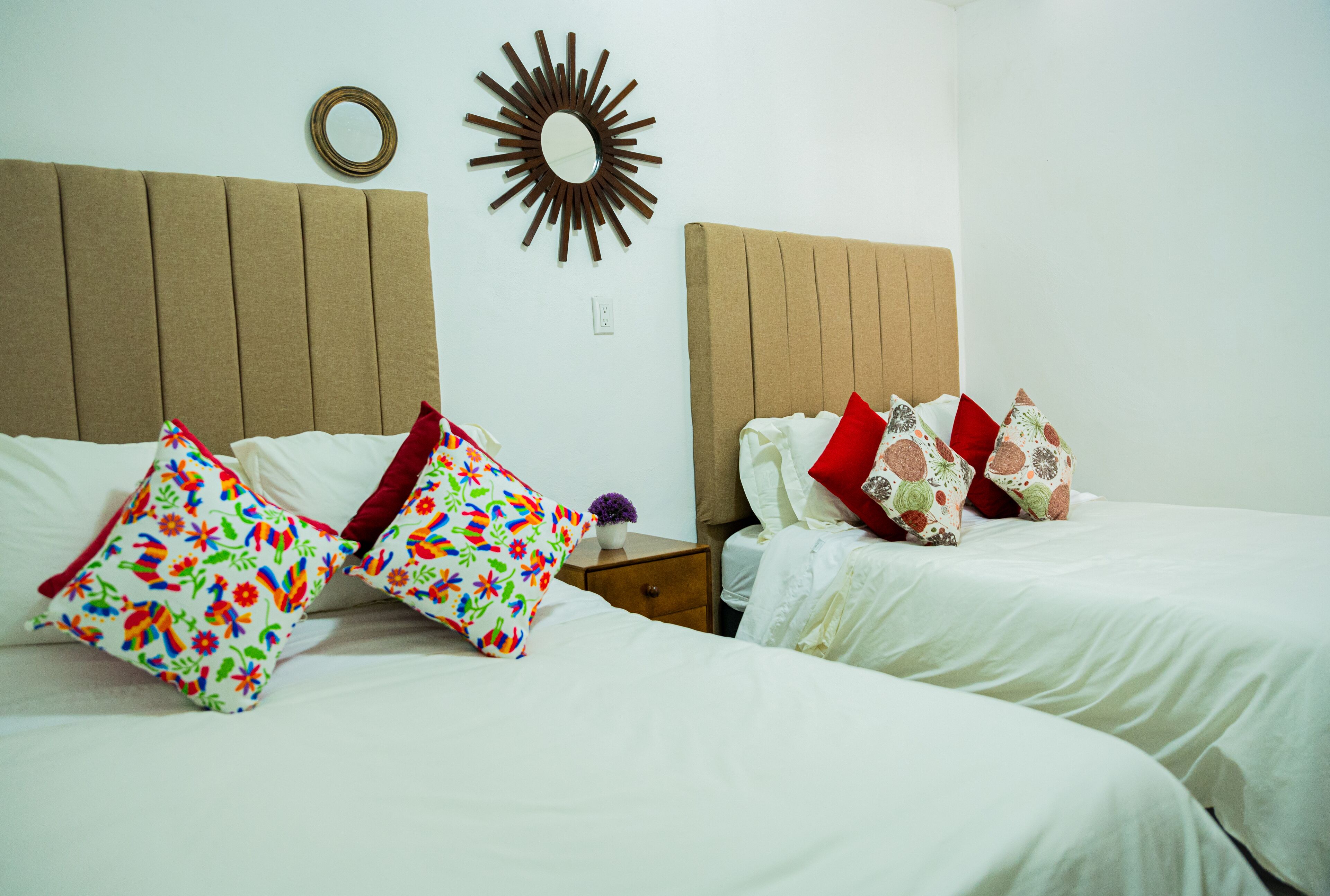 A hotel room with two beds, each with white bedding and colorful floral pillows.