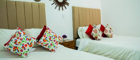 A hotel room with two beds, each with white bedding and colorful floral pillows.