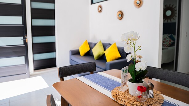 A modern living room with a dining table, a sofa with yellow cushions, and decorative wall art. - HOTEL BUNGALOWS CASA BLANCA (Tenancingo)