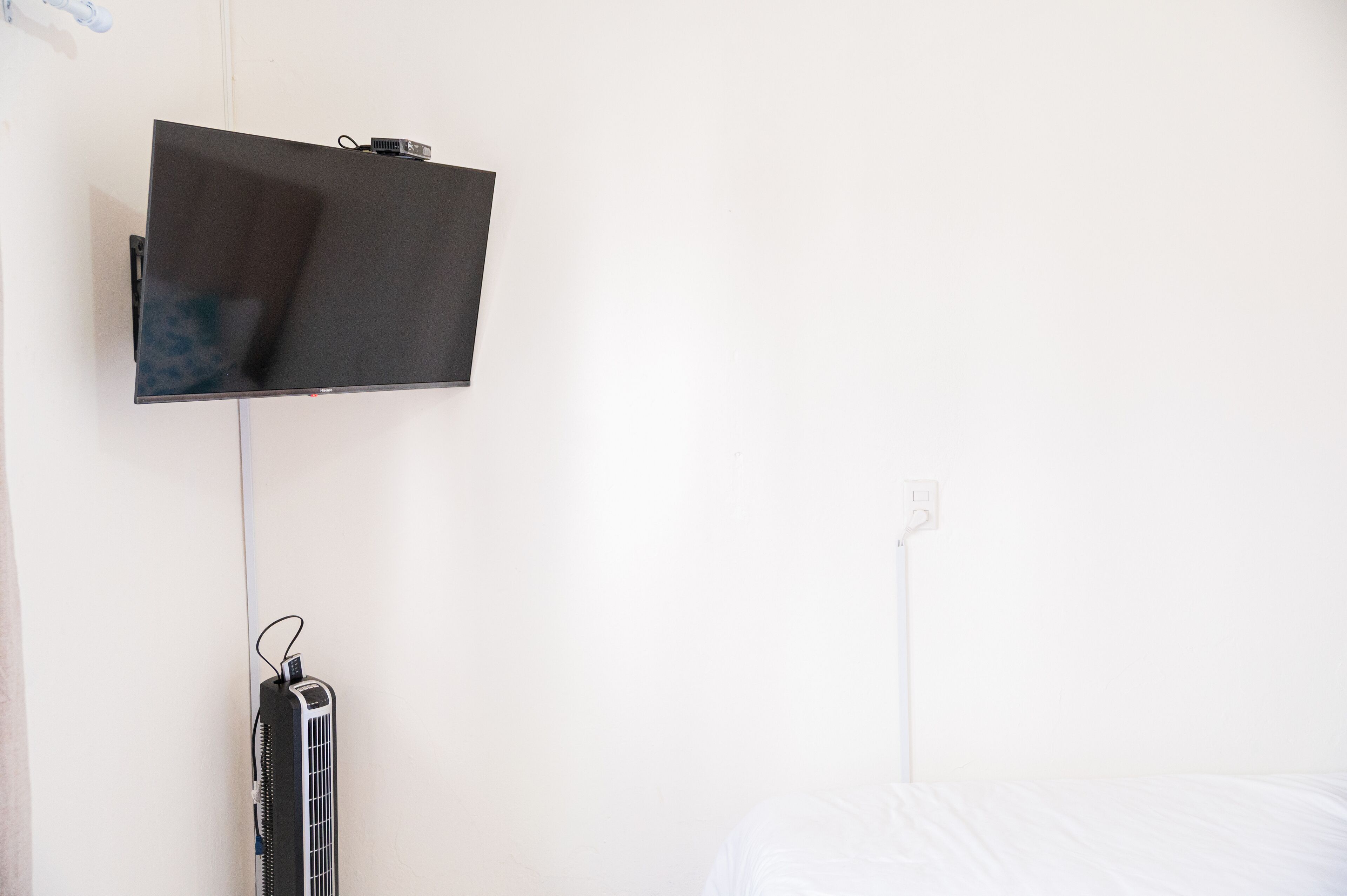 A wall-mounted television, a power outlet, and a wall-mounted heater in a room with white walls.