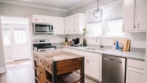A kitchen with white cabinets, a stainless steel dishwasher, a microwave, a stove, and a wooden island with a bench. - Walking Distance to Casino (Danvilel)