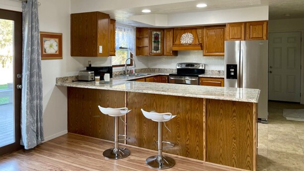 A modern kitchen with wooden cabinets, a granite countertop, stainless steel appliances, and two bar stools. - Extra clean home-free parking & Wi-Fi/self-check-in (Champaign)