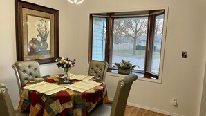 A dining area with a table covered by a colorful quilt, surrounded by four upholstered chairs. A vase with flowers is on the table, and a framed picture hangs on the wall. - Extra clean home-free parking & Wi-Fi/self-check-in (Champaign)