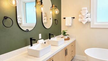 A modern bathroom with two sinks, a large mirror, and a bathtub.