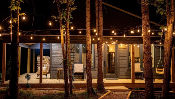Un espacio al aire libre cubierto con luces colgantes, una terraza de madera y asientos.