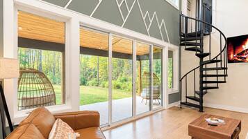 A spacious living room with a large window, a brown leather sofa, a wooden coffee table, and a black spiral staircase.