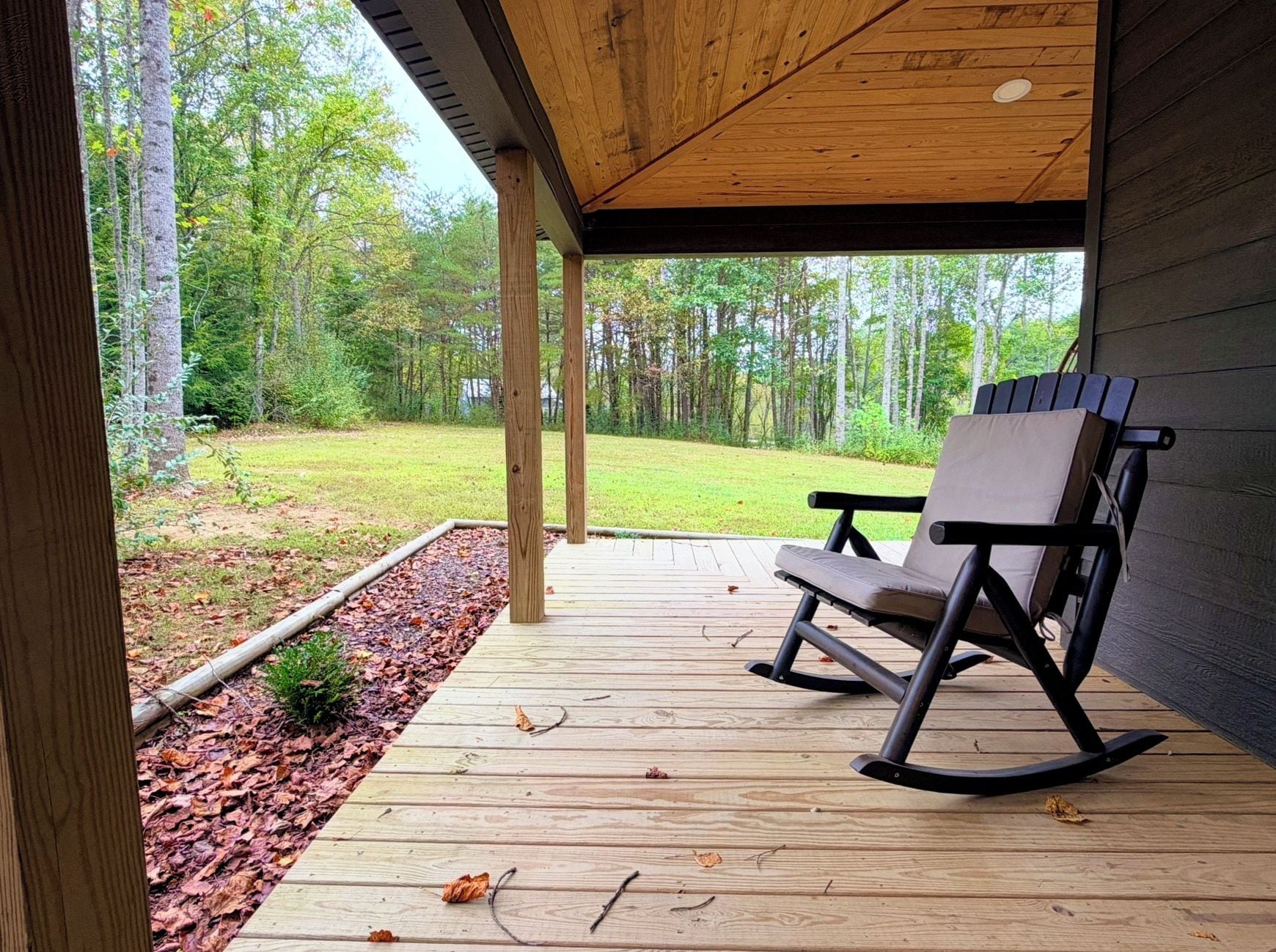 Une terrasse en bois avec un fauteuil à bascule, entourée d’une zone boisée.