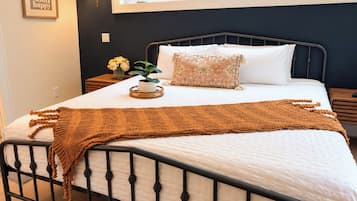 A bed with a white mattress, a brown knitted blanket, and a decorative pillow.