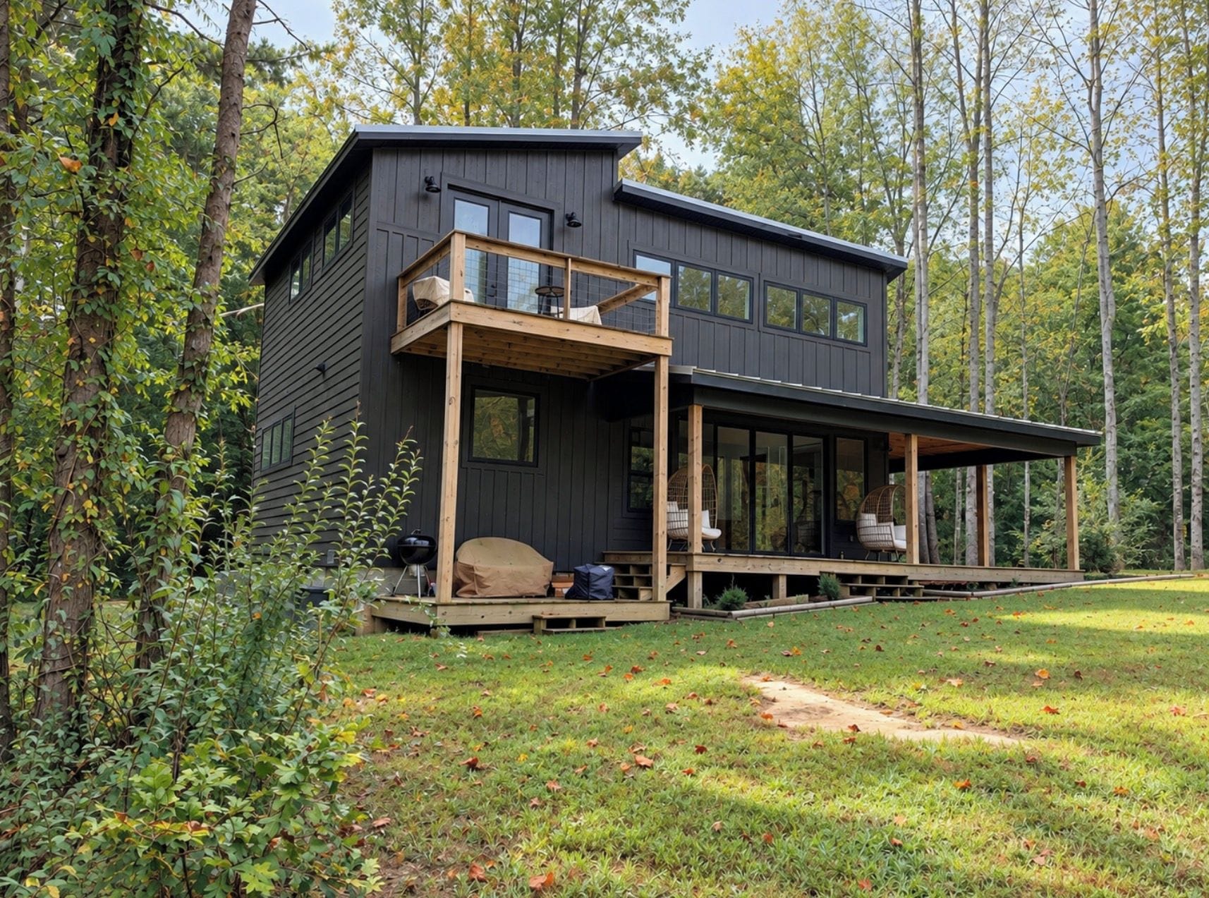 Une cabane moderne à deux étages, dotée d’une terrasse et entourée d’arbres.