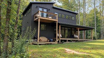 A modern two-story cabin with a deck, surrounded by trees.