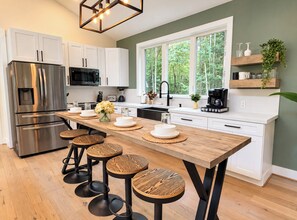 A modern kitchen with a central island, stainless steel appliances, and a view of greenery outside.
