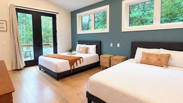 A bedroom with two beds, a wooden floor, a balcony door, and windows with a view of trees.