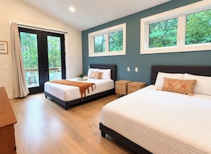 Un dormitorio con dos camas, piso de madera, puerta al balcón y ventanas con vistas a árboles.