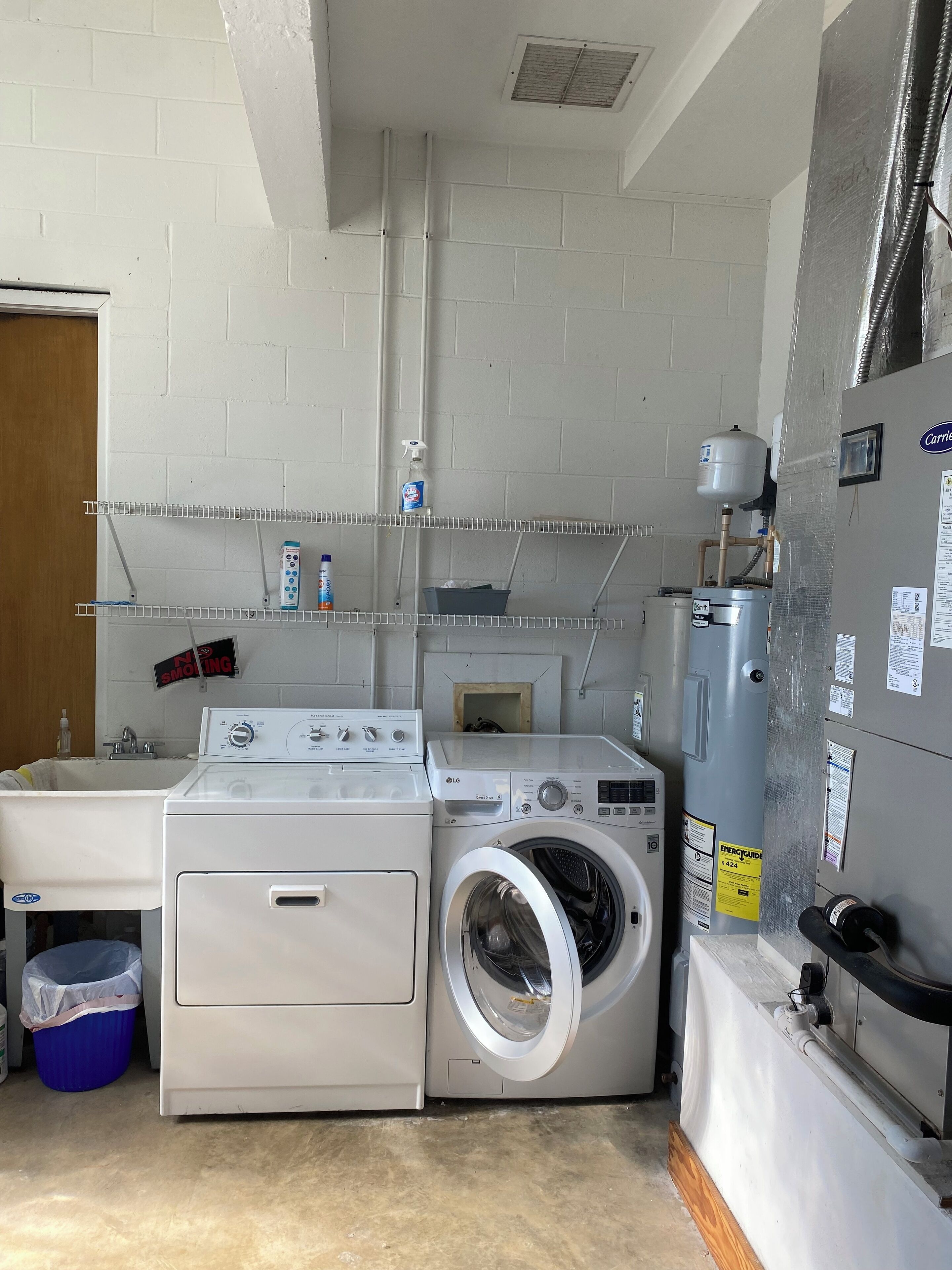 A laundry room with a washing machine, dryer, shelves with cleaning supplies, and a water heater.