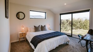 A bedroom with a large bed, a nightstand with a lamp, a window, and a view of the outdoors. - Minaret Ridge - Family friendly (Wanaka)