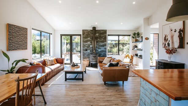 A spacious living room with a wooden dining table, leather sofas, and a kitchen area with a blue-painted cabinet. - Minaret Ridge - Family friendly (Wanaka)