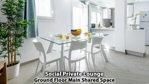 Een moderne, goed verlichte loungeruimte met een glazen tafel, witte stoelen en een schaal fruit.