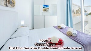 Dubbele kamer op de eerste verdieping met uitzicht op zee, voorzien van een terras, een bed, een nachtkastje, een schilderij en opgerolde handdoeken.