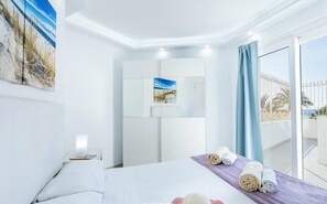 A first floor sea-view double room with a private terrace, featuring a bed, a nightstand, a painting, and rolled towels.
