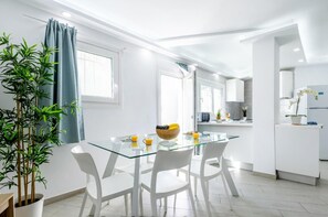 A modern, well-lit social private lounge with a glass table, white chairs, and a bowl of fruit.