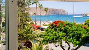 Blick aus einem Fenster auf einen Strand mit Palmen und einem Berg im Hintergrund.