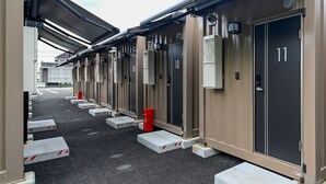 A row of hotel rooms with individual door numbers, a covered walkway, and a red trash bin. - HOTEL R9 The Yard Kasai (Kasai)