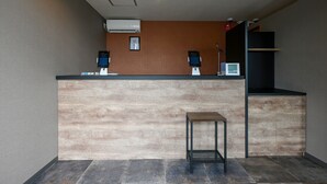 A reception area with a wooden reception desk, air conditioning unit, and a small table. - HOTEL R9 The Yard Kasai (Kasai)