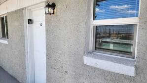 Fachada de edificio con una puerta blanca numerada con el número 4, una ventana que da a vistas de otro edificio y un accesorio de luz negro fijado a la pared.