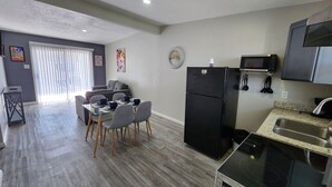 Una cocina moderna con un refrigerador negro, microondas y estufa. Hay un comedor con una mesa y sillas, y un sofá gris al fondo.
