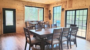 Un interior de madera con una gran mesa de comedor rodeada de sillas, ventanas amplias y techo de madera.