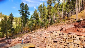 Una estructura de piedra con una plataforma de madera sobre un pequeño estanque, rodeada de árboles.