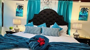A neatly made bed with a blue blanket and pillows, a decorative flower, and two wall-mounted lamps. - 2 bedroom Beach House at Bluefields Bay (Cave)