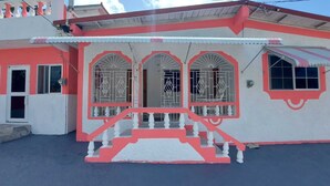 Un edificio con fachada roja y blanca, una entrada central con escaleras y ventanas arqueadas con celosías metálicas decorativas.