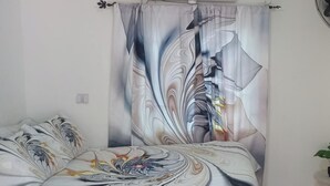 Un dormitorio con una cama, una cortina con diseño de mármol y una mesita con una planta.