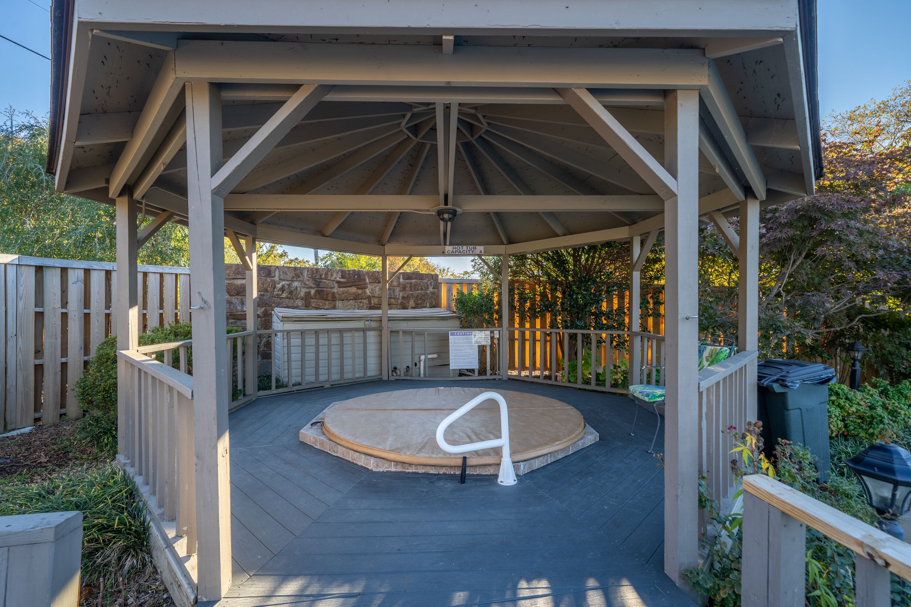 A covered patio area with a hot tub, wooden deck, and a small table.
