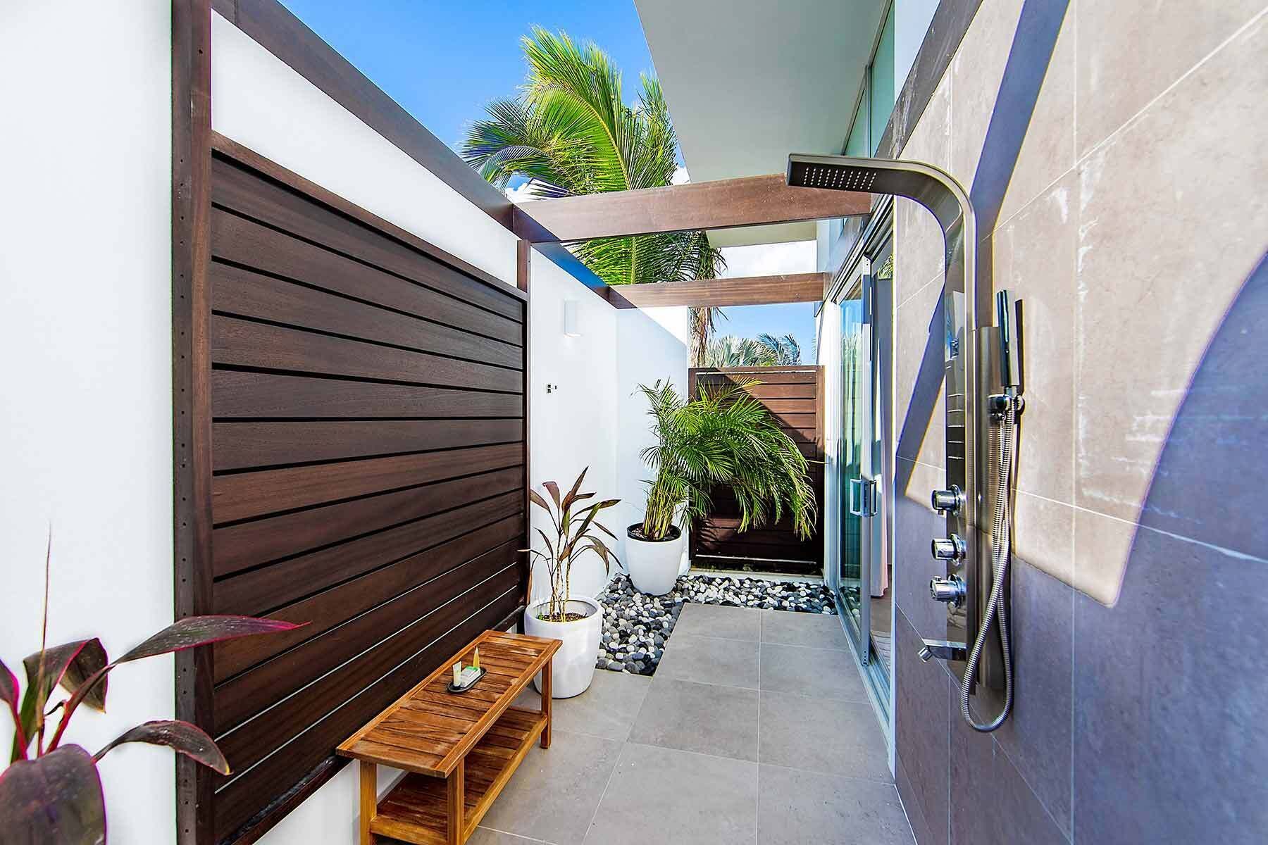 A narrow outdoor corridor with a wooden bench, potted plants, and a shower area.