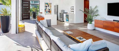 Ein modernes Wohnzimmer mit einer Couch, einem Couchtisch und einem Fernseher. Es gibt eine Küchenzeile mit einem Kühlschrank und einer Mikrowelle.