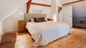 Une chambre à coucher avec un lit, des poutres en bois, une table de chevet, une lampe, un panier et un canapé.