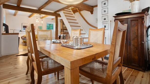 Une table à manger en bois, des chaises, un luminaire suspendu et un escalier en arrière-plan.