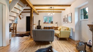 Un vaste espace de vie comprenant un escalier, des poutres en bois, un canapé, un fauteuil jaune et une vache allongée sur le sol.