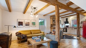 Un vaste espace de vie doté d’un plafond en bois, d’un canapé, d’une table basse avec des livres et d’une vue sur la cuisine.