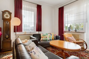 A living room with a sofa, a round table, a clock, and a window with curtains.