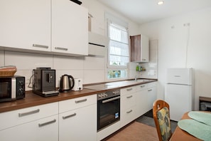 A modern kitchen with white cabinets, a built-in oven, a coffee maker, and a refrigerator.