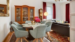 Un coin repas avec une table en bois, des chaises à revêtement gris, une chaise rouge, un buffet aux portes vitrées, une horloge et un lustre.