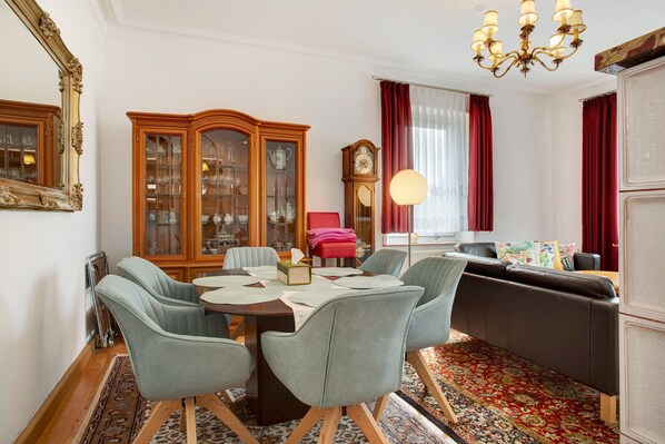 A dining area with a wooden table, grey upholstered chairs, a red chair, a cabinet with glass doors, a clock, and a chandelier.