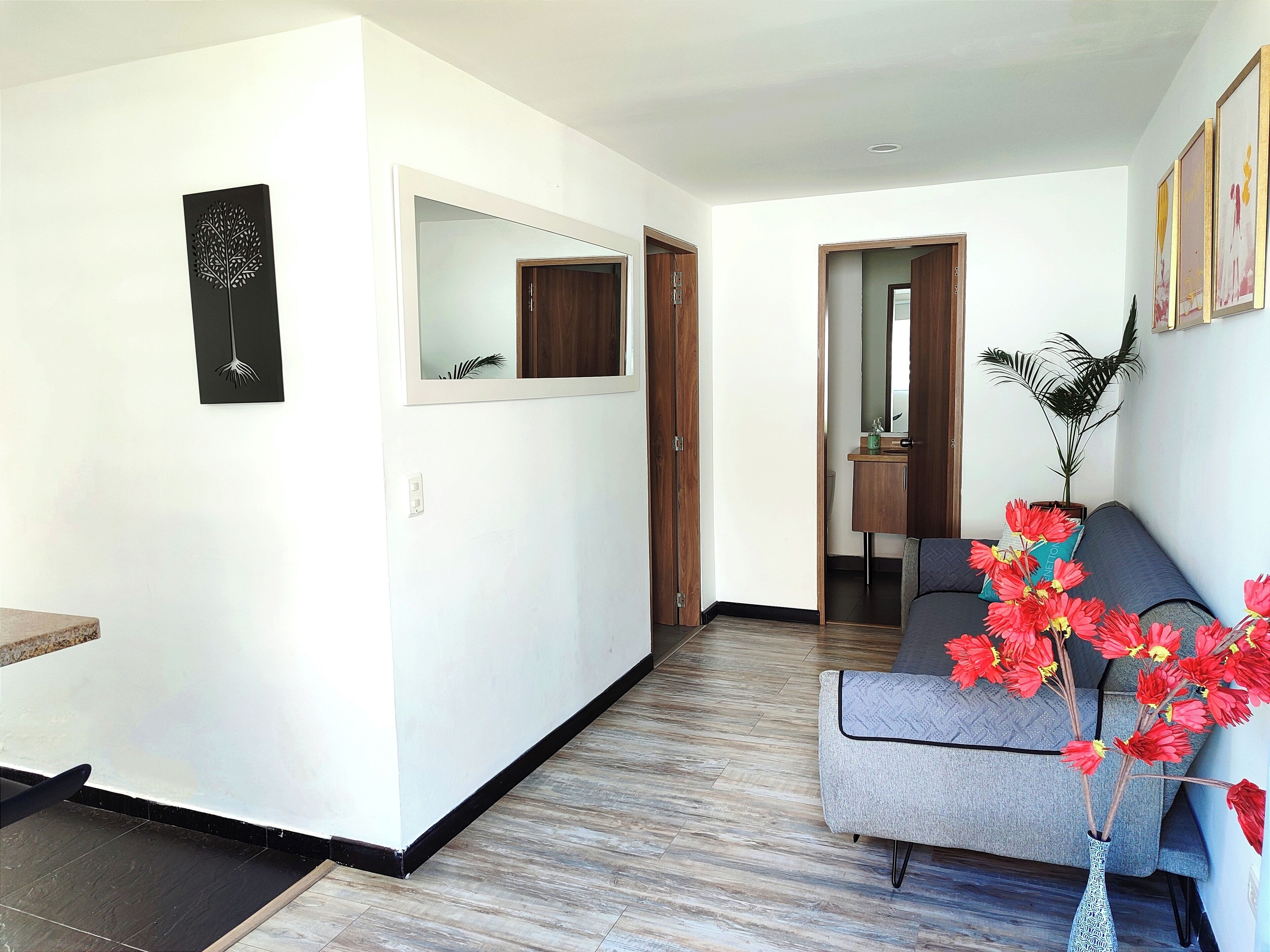Een moderne woonkamer met een grijze bank, een houten vloer en een vaas met rode bloemen.